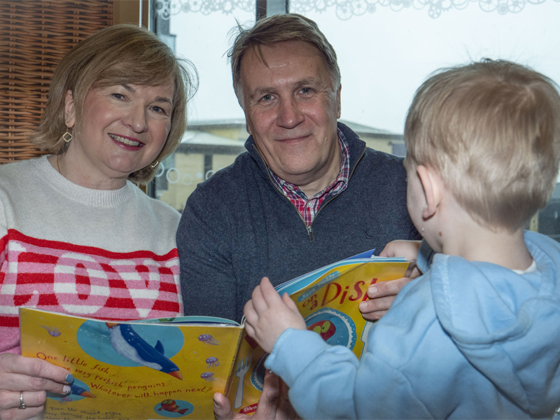 A picture of two foster carers reading to their foster child at home.